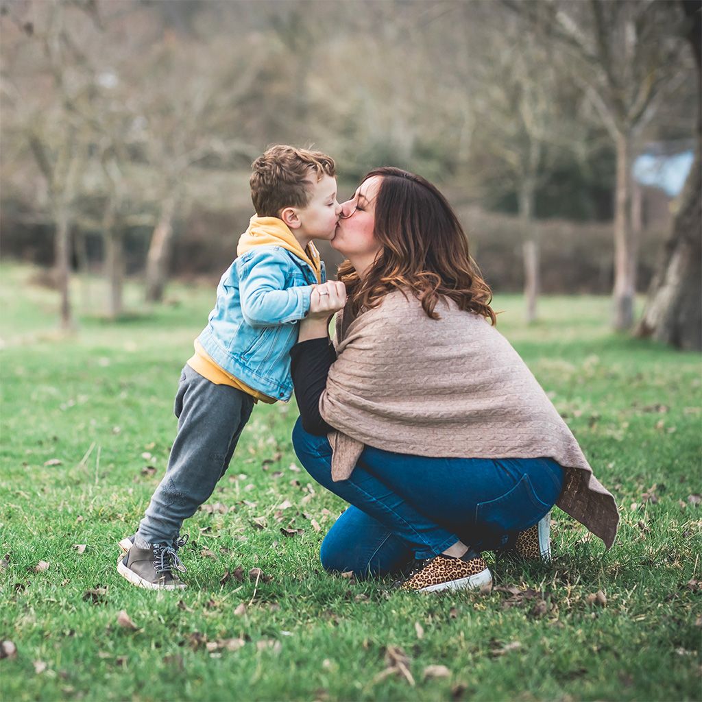 A happy photo of a mum kissing her son in a field in winter